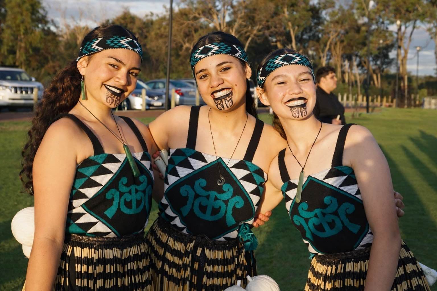 Three young wāhine smiling in kapa haka uniforms